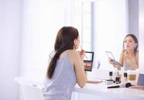 Mujer morena aplicando maquillaje para una cita nocturna frente a un espejo — Foto de Stock