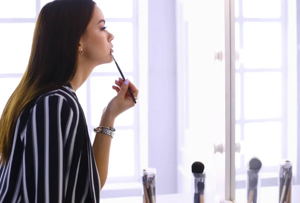 Young woman applying lipstick in front of a mirror — Stock Photo, Image