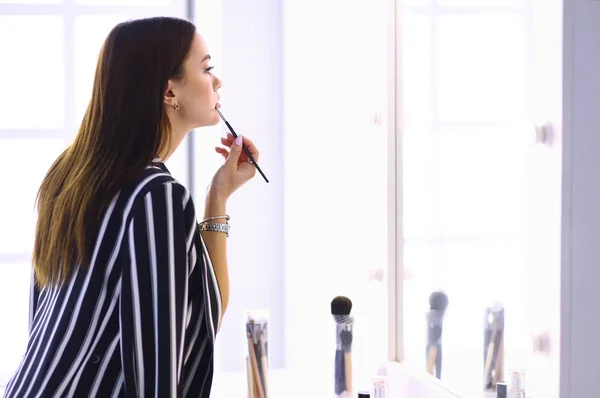 Jovem mulher aplicando batom na frente de um espelho — Fotografia de Stock