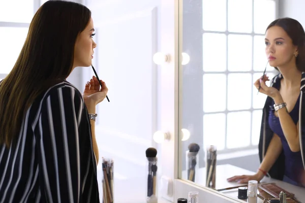 Mujer joven que aplica lápiz labial delante de un espejo — Foto de Stock