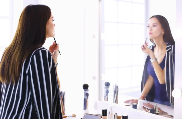 Young woman applying lipstick in front of a mirror — Stock Photo, Image