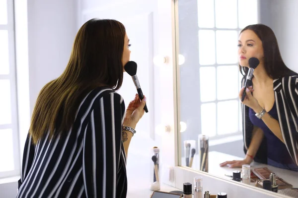 Skönhet kvinna tillämpa makeup. Vacker flicka ser i spegeln och tillämpa kosmetiska med en stor pensel — Stockfoto