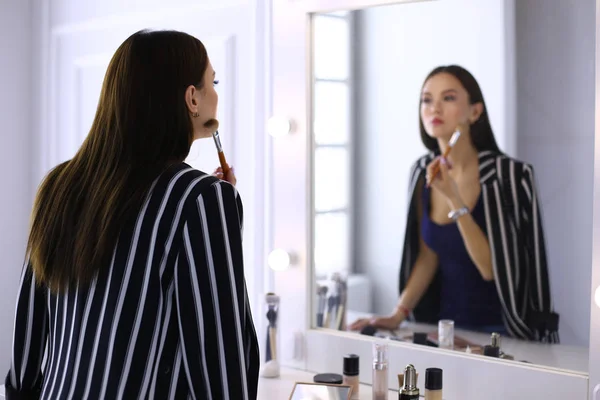 Красива дівчина дивиться у дзеркало і наносить косметику великою щіткою — стокове фото