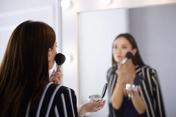 Schönheit Frau beim Schminken. schönes Mädchen, das in den Spiegel schaut und Kosmetik mit einem großen Pinsel anwendet — Stockfoto