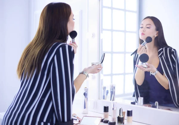 Hermosa chica mirando en el espejo y la aplicación de cosméticos con un cepillo grande —  Fotos de Stock