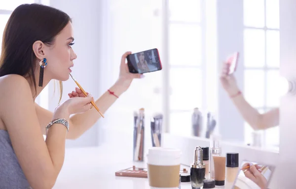 Blogger de belleza filmando tutorial de maquillaje con teléfono inteligente frente al espejo —  Fotos de Stock