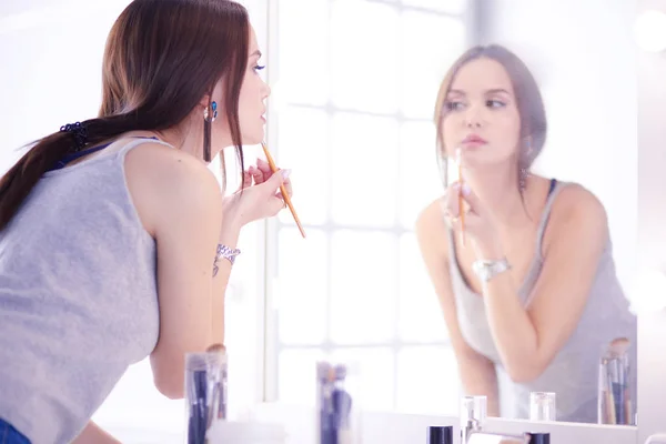 Young woman applying lipstick in front of a mirror — Stock Photo, Image