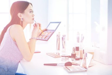 Esmer bir kadın aynanın önünde akşam randevusunu telafi etmek için başvuruyor.