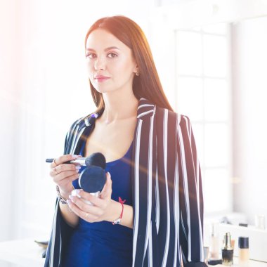 Makyaj fırçası yüzüne yakın bir kadın portresi.