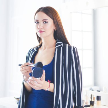 Makyaj fırçası yüzüne yakın bir kadın portresi.