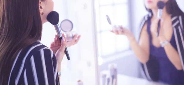 Schönes Mädchen, das in den Spiegel schaut und Kosmetik mit einem großen Pinsel anwendet — Stockfoto