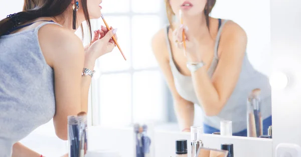 Young woman applying lipstick in front of a mirror — Stock Photo, Image