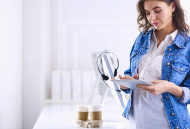 Gülümseyen kadın kahve içiyor ve kafede tablet kullanıyor.