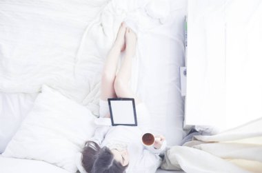 Sabahları yatakta otururken tablet kullanan ve kahve içen kadın portresi