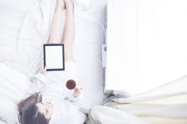 Sabahları yatakta otururken tablet kullanan ve kahve içen kadın portresi