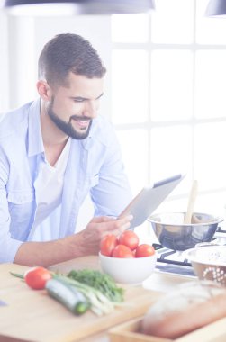 Dijital tablet ve yemek pişirme tarifine uyan bir adam evdeki mutfakta lezzetli ve sağlıklı yemekler pişiriyor.