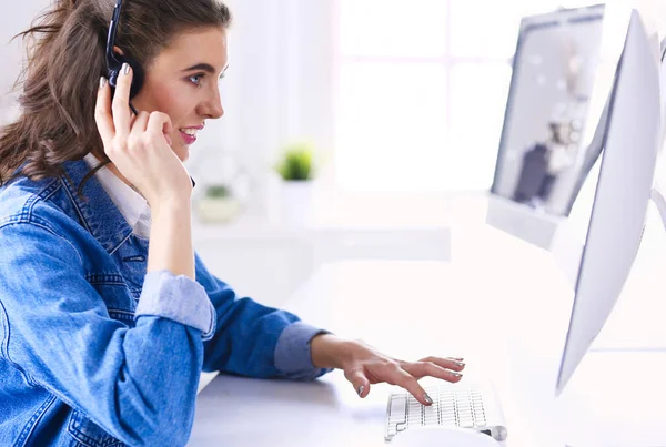 Feliz encantadora joven sentada y trabajando con el ordenador portátil con auriculares en la oficina —  Fotos de Stock