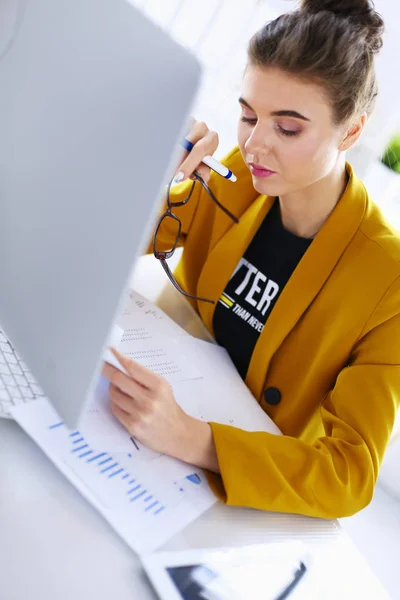 Mujer atractiva sentada en el escritorio en la oficina, trabajando con computadora portátil, sosteniendo el documento — Foto de Stock