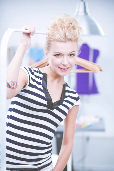 Hermosa joven estilista cerca de rack con perchas en la oficina —  Fotos de Stock