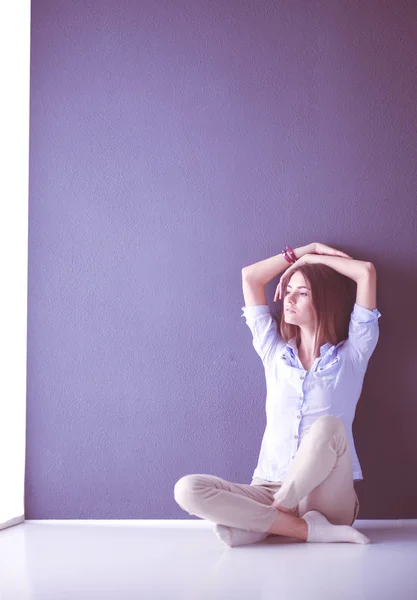 Portrait of a casual happy woman sitting on the floor on gray background — Stock Photo, Image