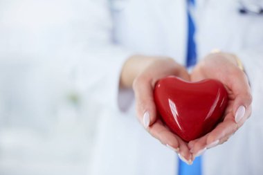 Steteskop tutan, kalbi hafif arka planda olan kadın bir doktor.