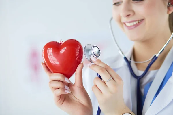 En läkare med stetoskop undersöker rött hjärta, isolerad på vitt — Stockfoto