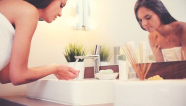 Genç bir kadın banyoda yüzünü temiz suyla yıkıyor.