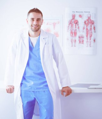 Genç ve kendinden emin erkek doktor portresi tıp ofisinde duruyor.