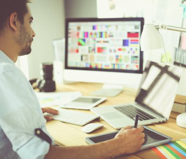 İnternette çalışırken bilgisayarın ve dizüstü bilgisayarın önünde grafik stüdyosunda oturan genç tasarımcının portresi