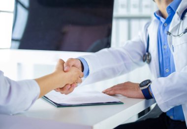 Yakışıklı doktor genç bayan hastasıyla konuşuyor ve ofisinde otururken notlar alıyor.