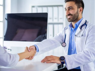 Doktor masadaki hastaya el sıkışıyor.