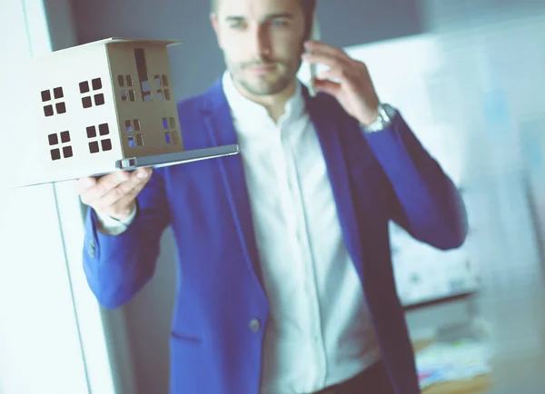 Homme d'affaires tenant maison miniature à portée de main debout dans le bureau . — Photo
