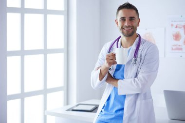 Genç ve kendinden emin erkek doktor portresi tıp ofisinde duruyor..