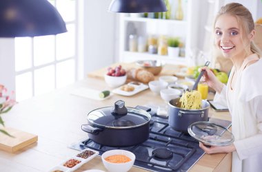 Evdeki mutfakta yemek pişiren güzel genç bir kadın.