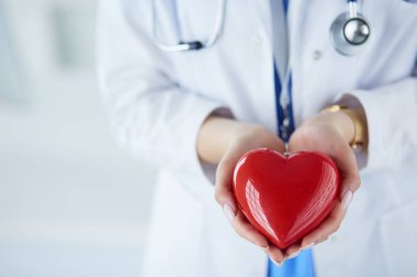 Steteskop tutan, kalbi hafif arka planda olan kadın bir doktor.