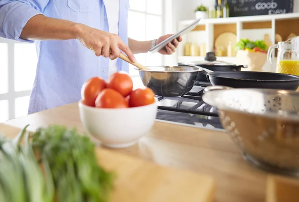 Man following recipe on digital tablet and cooking tasty and healthy food in kitchen at home — Stock Photo, Image