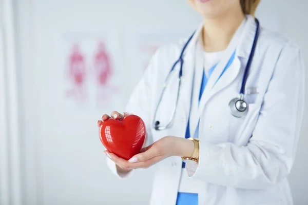 Médica com estetoscópio segurando coração, em fundo claro — Fotografia de Stock