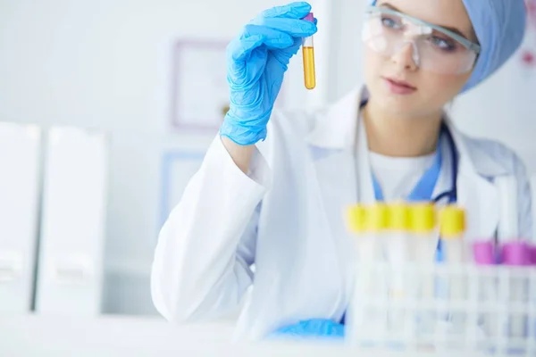 Női orvos- vagy tudományos kutató vagy női orvos, aki egy laboratóriumban tiszta oldatot tartalmazó kémcsövet néz — Stock Fotó
