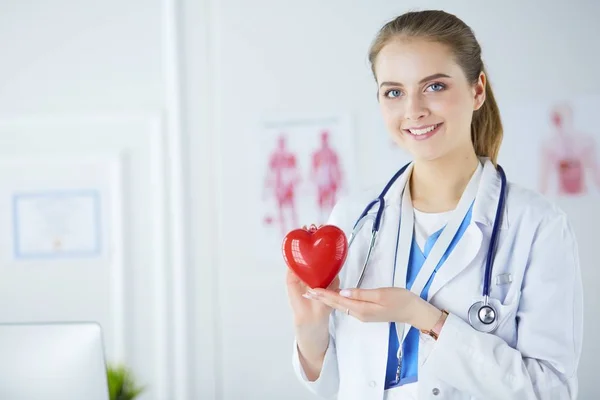 Médica com estetoscópio segurando coração, em fundo claro — Fotografia de Stock