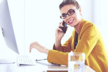 İş kadını ofiste bilgisayar ve cep telefonu kullanarak işine konsantre oluyor.