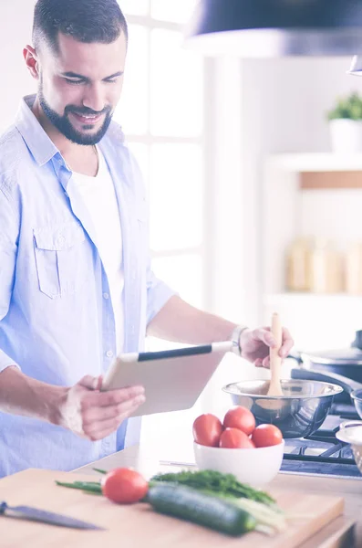 Man following recipe on digital tablet and cooking tasty and healthy food in kitchen at home