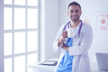 Genç ve kendinden emin erkek doktor portresi tıp ofisinde duruyor..