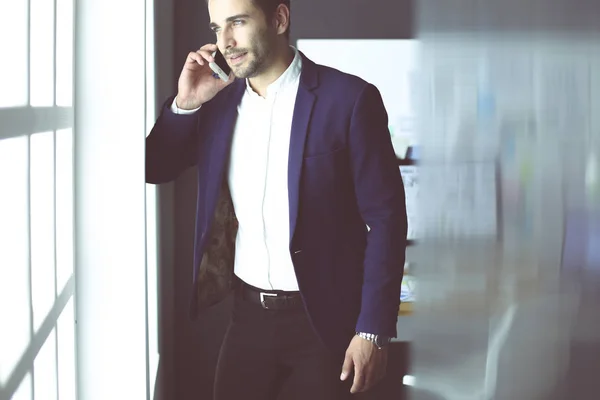 Affärsman i kostym prata telefon och tittar bort nära fönstret. — Stockfoto