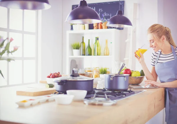 Приваблива жінка тримає стакан апельсинового соку, стоячи на кухні — стокове фото