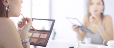 Esmer bir kadın aynanın önünde akşam randevusunu telafi etmek için başvuruyor.