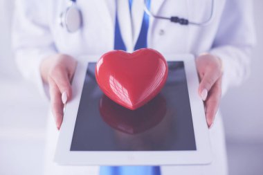 Steteskop tutan, kalbi hafif arka planda olan kadın bir doktor.