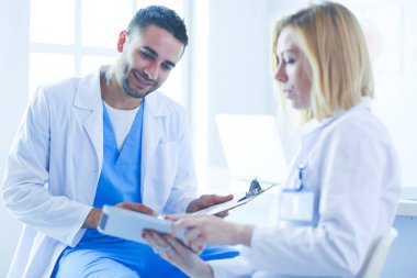 Yakışıklı doktor genç bayan doktorla konuşuyor ve ofisinde otururken notlar alıyor..