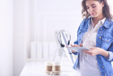 Gülümseyen kadın kahve içiyor ve kafede tablet kullanıyor.