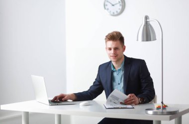 Beyaz arka plan üzerinde beyaz bir dizüstü bilgisayar ile beyaz masada oturan iş adamı