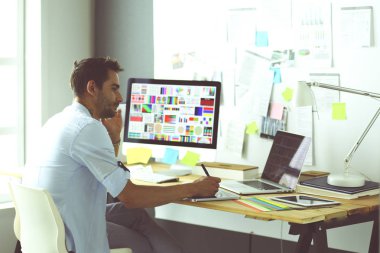 İnternette çalışırken bilgisayarın ve dizüstü bilgisayarın önünde grafik stüdyosunda oturan genç tasarımcının portresi.